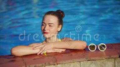 红头发的女人在游泳池里放松。 她站在游泳池旁边
